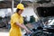 Asian automotive mechanic girl with yellow suit and helmet check the engine and system of the car during day time