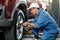 Asian automotive mechanic with white cap and blue uniform is working with replace or fix the problem of car wheel in the garage