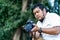 Asian beard Thai professional camera man check image shot via liveview behind Medium format Mirrorless camera with green tree
