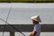 An asian boy with conical hat  fising on a bridge