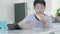 Asian boy doing homework at home with a happy expression While in the hand holding the food