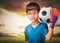 Asian boy is football goalkeeper wearing gloves and holding a soccer ball with cloud sky background