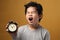 Asian boy holding alarm clock and yawning, sleepy tired young kid, late wake up