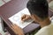 Asian boy learning and practicing to draw 3D shapes on drawing notebook on brown desk at home