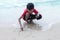 Asian boy sitting and drawing a house on the sand beach while going on vacation.