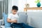 Asian boy sitting open notebook, studying online morning, sitting on living room sofa house, looks determined to study, When class