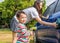 Asian boy washing blue car by green water sprayer