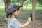 An Asian boy wearing a hat in a forest exploration suit plays with a beetle clinging to a tree