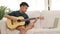 Asian boys live at home. sitting on white sofa Holding a guitar to learn music online
