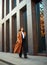 Asian business woman in long beige coat and hat walks down modern street on background of building in urban style