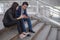 Asian businessman and businesswoman sit on the staircase and using telephone to surf internet for shopping online.