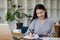 Asian businesswoman holding a smartphone analyzing a report pointing to a graph with a pen, laptop, and calculator. in workstation