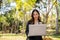 An Asian businesswoman working in a park, sitting on a bench, sipping coffee, and using laptop