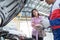 Asian car mechanic and customer Woman talking to a car mechanic in Car service center, both are standing next to the car