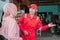 Asian car washer wearing red uniform standing smiling inviting customers to wait