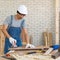 Asian carpenter with a hard hat and dustproof glasses use a sander machine to smooth plywood surface by abrasion with sandpaper.
