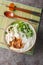 Asian chicken noodle soup with fried onions, green onions and cilantro close-up in a bowl. Vertical top view