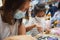 Asian child girl and her mother wearing protection mask making fusible beads thermo mosaic in pegboard that is a toy to develops