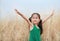 Asian Child girl with outstretched arms in the dried grass field. Rear view