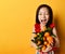 Asian child in red blouse. Looking wondered, holding an armful of tangerines and oranges, posing on orange background. Close up