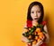 Asian child in red blouse. Looking wondered, holding an armful of tangerines and oranges, posing on orange background. Close up