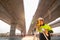 Asian civil engineer or surveyor holding a blueprint and making measuring under the expressway with theodolite on road works.