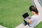 Asian college student or freelance woman using laptop on stairs in university campus or modern park