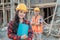 Asian construction worker woman smiles at the camera wearing a safety helmet against the background of a male contractor