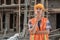 An Asian contractor stands wearing a safety helmet and vest with a gesture of getting into trouble