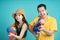Asian couple holding plastic water guns happy for Songkran festival, isolated on blue background