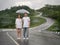Asian couple holding umbrella on extremely curved road in mountain. Nan, Thailand. sky road on hill.