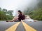 Asian couple sitting back against back on road center line. road on mountain in foggy day.