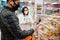 Asian couple wear in protective face mask shopping together in supermarket during pandemic. Man use smartphone for quick purchase