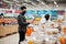 Asian couple wear in protective face mask shopping together in supermarket during pandemic. Man use smartphone for quick purchase