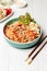 Asian cuisine. Funchosa with vegetables, mushrooms and meat. Close-up. On a light wooden table with chopsticks