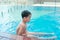 Asian cute child swimming in swimming pool. He playing is funny on summer holiday on blurred background. Cute boy smile and swim