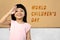 Asian cute girl with a funny expression standing with world children`s day text on the wall