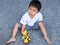 Asian cute little child boy playing yellow car toy outdoor with dirty foot