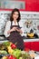 Asian cute middle-age woman in an apron stading using mobile smartphone connect to internet in kitchen with a smiling face and