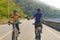 Asian cyclist man handing water bottle to his female cyclist girlfriend to drink water. While doing exercise together in the