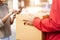 An Asian deliver man in red uniform handing parcel to a female costumer in front of the house. A postman and express delivery