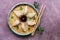 Asian dumplings on a plate with soy sauce, sesame seeds, greens, chopsticks on a rustic purple background. Traditional Chinese foo