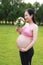 Asian Eastern Chinese happy pregnant woman in yoga dress hands hold her belly expecting baby to born smell flowers hold bouquet