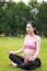 Asian Eastern Chinese pregnant woman do yoga the lotus pose sit in meditation in nature outdoor sit on green grass meadow park