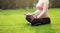 Asian Eastern Chinese young pretty pregnant girl woman do yoga sit in meditation, do lotus gesture of yoga in outdoor nature sun