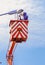 Asian electrician in bucket boom truck is repairing street lamppost against blue sky in vertical frame