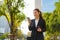 Asian executive working woman holding coffee cup and using a mobile phone in the street with office buildings in the background in