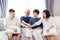 Asian family with adult children and senior parents putting hands together and sitting on sofa at home together. Family unity