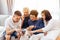 Asian family with adult children and senior parents using a mobile phone and relaxing on a sofa at home together.