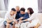 Asian family with adult children and senior parents using a mobile phone and relaxing on a sofa at home together.